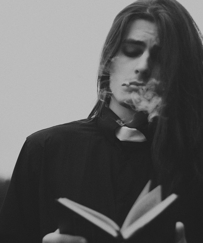 Black and white photo, lith a pastor reading from a book. they have long hair and looks like there is smoke around his mouth